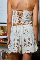 Short blanco de tela calada con diseño de palmeras y frutos, con broche de gancho y cierre. Terminación en puntilla y calce holgado en las piernas.