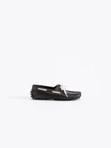 Mocasín Lyon de cuero vacuno color marrón oscuro con efecto gastado. Presenta detalles de picado en los laterales y la capellada, y se ajusta con cordones de encaje blancos. Suela de goma.