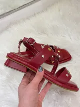 Sandalias rojas de cuero con tiras cruzadas y detalle de tachas plateadas y doradas.