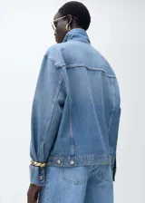 Chaqueta de jean celeste de corte oversize, con cuello camisero, cierre frontal con botones metálicos, dos bolsillos de parche con botón en el pecho y dos bolsillos laterales.