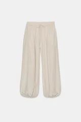 Pantalón bombacho color beige confeccionado en tejido fluido, con cintura elástica ajustable con cordones y bajo abullonado con elástico interior.