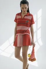 Remera polo tejida a rayas horizontales rojas y rosadas, con cuello clásico y bordado de ají verde.