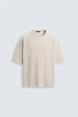 Camiseta color beige de punto tejido en hilatura de algodón, corte relaxed fit, cuello redondo, manga corta, efecto lavado y acabados irregulares.