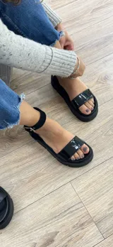 Sandalias negras con plataforma track y tira ancha sobre los dedos. Presentan una tira con hebilla alrededor del tobillo.