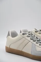 Zapatillas urbanas de cuero color crema con detalles en gris y suela de goma marrón.