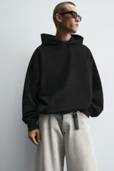 Sudadera negra de tejido con textura acanalada, corte boxy, capucha con cordón ajustable, manga larga con puños acanalados y bajo con elástico.