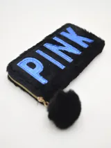 Billetera rectangular de piel sintética color negro, con textura de pelo sintético y cierre de cremallera dorada. Tiene bordado el nombre "PINK" en letras azules. Incluye un pompón de pelo sintético negro.