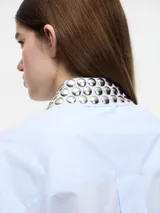 Camisa celeste cropped con tachas en el cuello y puños, con botones en la parte delantera y en los bolsillos. Tiene pinza en la parte trasera.