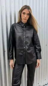 Camisa negra de cuero ovino italiano, con mangas largas, hombros caídos y calce oversize. Tiene cierre frontal con broches metálicos.
