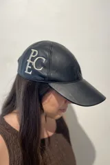 Gorra de cuero ovino color camel, confeccionada a mano, con bordado del monograma "PEC" en hilo blanco en el lateral.