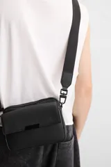 Bandolera negra con textura grabada, compartimento principal con cierre de cremallera, bolsillo interior con cremallera, bolsillo frontal con solapa y cremallera, asa de hombro removible y ajustable.