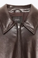 Chaqueta bomber de efecto piel color marrón oscuro, con cuello solapa, manga larga con elástico interior y bajo elástico. Incluye bolsillos de vivo en el delantero y cierre frontal con cremallera metálica.