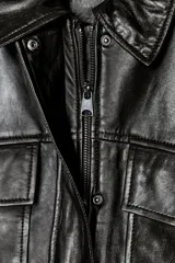 Cazadora negra de cuero con cuello solapa, manga larga con trabilla y bolsillos de parche con solapa en el delantero. Cierre frontal con cremallera y botones a presión ocultos por solapa.