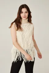 Chaleco color crema de punto con cuello alto y flecos en el ruedo.