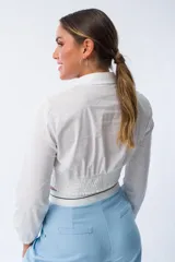 Camisa blanca de algodón y elastano, con corte cropped, cuello clásico, mangas largas con puños elásticos y cintura ajustada con elástico.