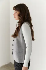 Chaleco gris de tejido de punto con cuello en V, cierre frontal con botones y bolsillos delanteros.