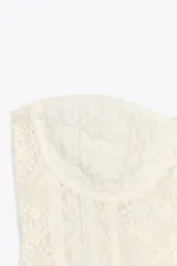 Corsé sin mangas color blanco roto, confeccionado en encaje floral, con escote recto y aros. Presenta cierre frontal con ganchos metálicos.