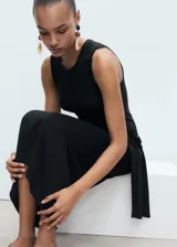 Vestido midi negro, sin mangas, con cuello redondo y tirantes anchos. Presenta un nudo decorativo en la cintura que cae como un lazo.