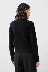 Chaqueta tejida negra con botones dorados, de corte clásico y mangas largas.