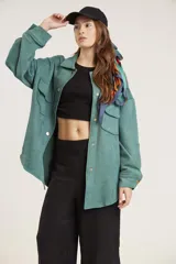 Sobrecamisa verde con botones dorados, bolsillos delanteros y pañuelo estampado atado al cuello.