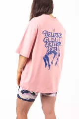 Remera oversize rosa con estampado en la espalda que incluye texto y una ilustración de dos personas cayendo.