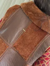 Chaleco marrón con cierre frontal, cuello de piel sintética y diseño patchwork con bloques de cuero y piel sintética.
