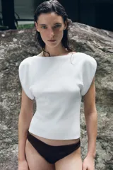 Top blanco ajustado de cuello redondo amplio y manga corta con cremalleras plateadas en los hombros.