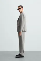 Pantalón de vestir gris claro, de corte recto, confeccionado en tejido con lana. Cuenta con bolsillos frontales y traseros de doble vivo con botón. Cierre frontal con cremallera y botón.