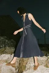 Vestido midi azul marino con estampado de lunares blancos, cuello solapa, escote en pico y sin mangas. Incluye cinturón de la misma tela y cierre frontal con botones.