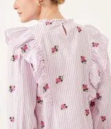 Blusa de algodón a rayas verticales blancas y lilas, con bordado de rosas rosadas. Tiene cuello redondo con volados, mangas largas y volados en los hombros.