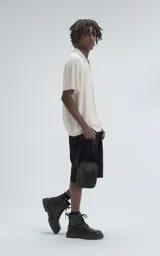 Camisa de tejido de punto color beige, manga corta, con cuello polo y cierre frontal de botones. Presenta un calce regular y un patrón calado en zigzag.