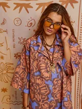 Camisa oversize de algodón con estampado abstracto en tonos marrón, naranja y celeste. Tiene cuello clásico, cierre frontal con botones y mangas cortas.