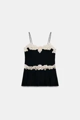 Top negro con escote pico y tirantes finos. Presenta detalles de encaje calado color crema en el escote y a la altura de la cintura, con una caída plisada en la parte inferior.