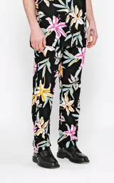 Pantalón recto unisex con estampado floral en tonos rosa, amarillo, celeste y blanco sobre fondo negro. Confeccionado en rayón.