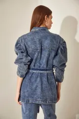 Campera de denim celeste con efecto nevado, corte recto, cuello clásico, cierre frontal con botones metálicos, cuatro bolsillos frontales con solapa y cinturón de la misma tela con hebilla metálica.