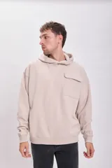 Canguro deportivo color beige con capucha, corte holgado y bolsillo tipo parche en el pecho.
