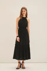 Vestido largo negro con escote halter con volados en cuello y fuelle con cinta interna para ajustar escote. Tiene volados y costuras elásticas en cintura y ruedo con volado.