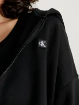 Buzo negro cropped con capucha y cierre frontal, de felpa de mezcla de algodón regenerativo y poliéster reciclado. Tiene puños y bajo de canalé e insignia de Calvin Klein Jeans bordada en el pecho.