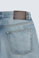 Jeans de denim de algodón, tiro medio, con pierna recta y ajuste relajado. Presentan un efecto lavado claro y cierre frontal con botones.