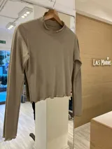 Remera gris de morley de algodón, de manga larga, con terminaciones fruncidas en cuello y mangas.