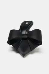 Zapato de tacón tipo mule color negro, con punta fina, tacón fino alto y maxi lazo decorativo en la parte delantera.