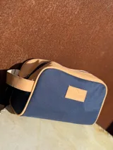 Nécessaire azul marino de lona con detalles en cuero color beige, cierre superior con cremallera y asa lateral.