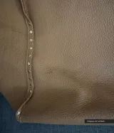 Bolso tipo tote de cuero color beige con textura granulada y tachas plateadas en los laterales.