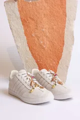 Zapatillas bajas color crema con detalles de cuero sintético y apliques de dijes dorados en los cordones.