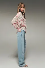 Camisa semitransparente con estampado de flores en tonos rosa y verde, cuello pico y manga larga con puños. Tiene aberturas laterales y cierre frontal con botones.