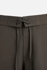 Pantalón marrón oscuro de corte amplio, con cintura ajustable con cordón, bolsillos plastrón delanteros y traseros, detalle de costuras frontales y cierre frontal con cremallera y gancho metálico oculto.