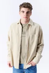 Sobrecamisa beige de pana con cuello clásico, cierre frontal con botones, mangas largas con puños abotonados y dos bolsillos de parche en el pecho.
