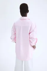Camisa rosa de algodón Oxford con cuello clásico, botones al frente, canesú con trabilla en la espalda, corte relajado, hombros caídos, mangas largas con puños sencillos, bolsillos superiores con solapa y bajo redondeado con espalda más larga.