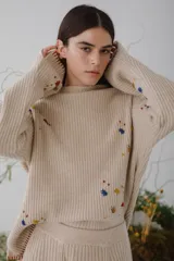 Sweater beige de lana con cuello redondo y mangas largas. Presenta detalles de bichos tejidos a contratono en la parte superior delantera.