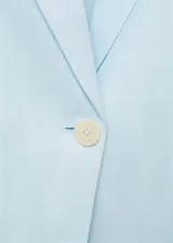 Chaqueta de lino color celeste con cuello de pico y solapas con muesca, cierre frontal con botón, manga larga con puños abotonados, diseño recto, dos bolsillos de ribete en la parte delantera y abertura posterior en el bajo.